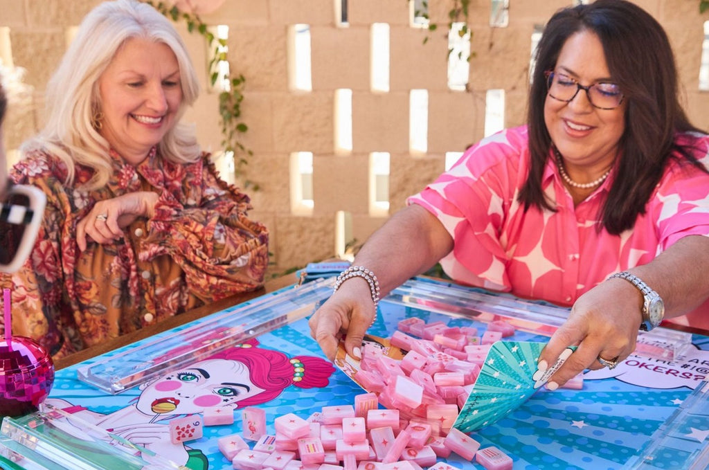 Two women playing with Pop Diva Cotton Candy Pink Pearl tiles on clear racks; racks and mat sold separately