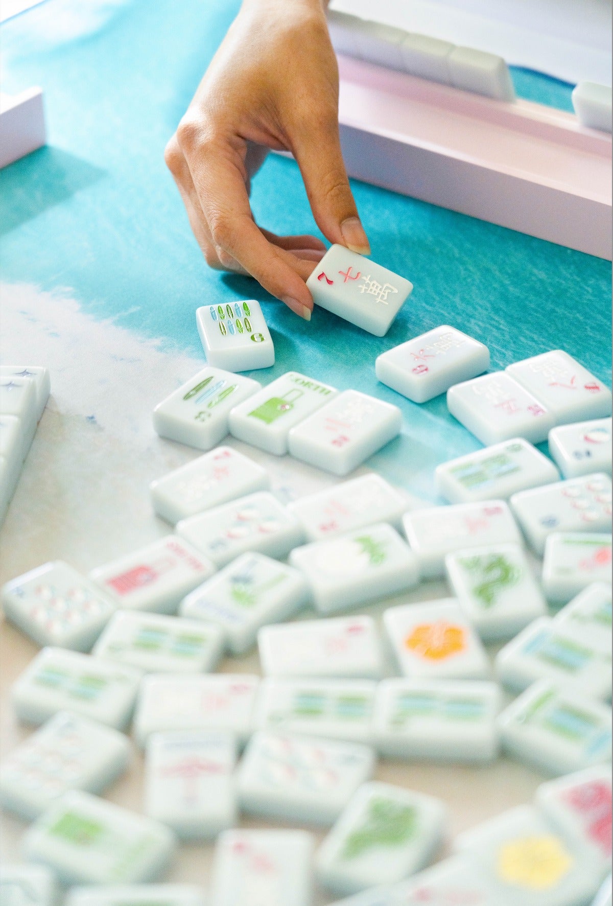 Hand picking up a Springtime Safari Bright White tile from a spread of tiles on a blue mat; mat sold separately