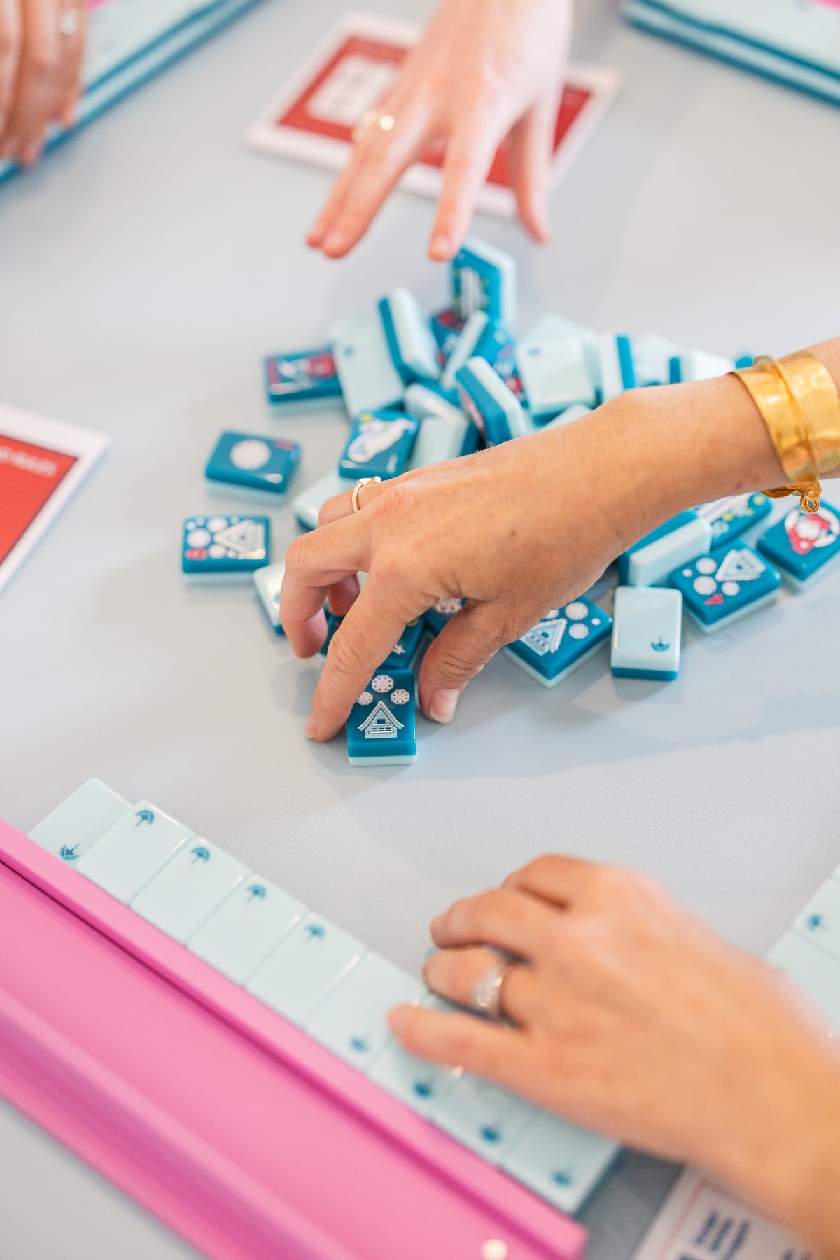 Players mixing Après Ski Club tiles on a table with pink racks; racks and mat sold separately