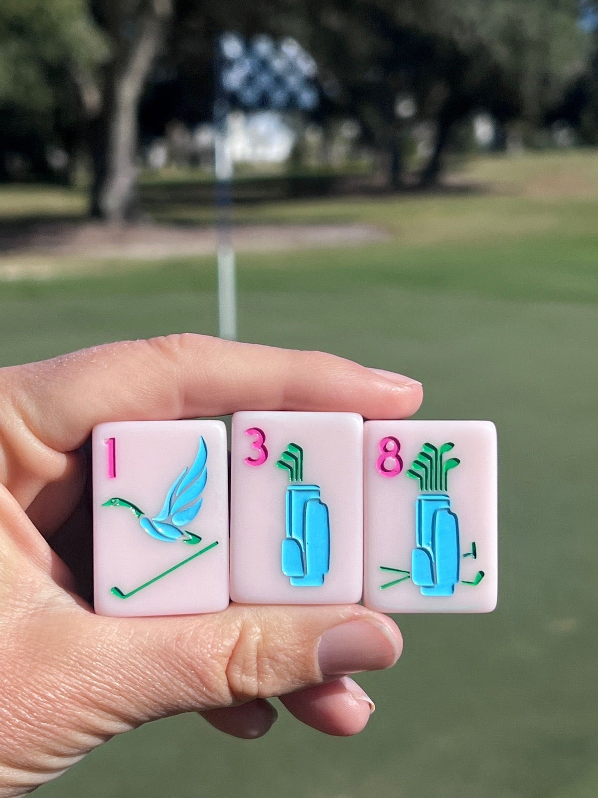 Three Country Club tiles held up on a golf course: the flying-duck one bam and two golf-bag bams