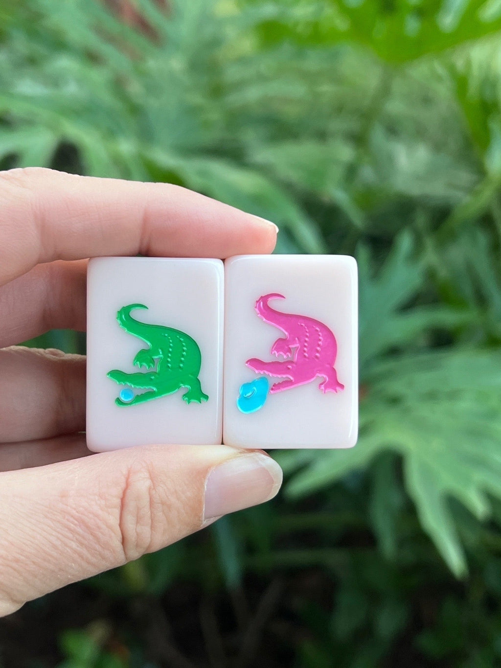 Two Country Club dragon tiles held in hand, a green gator and a pink gator with a blue golf ball