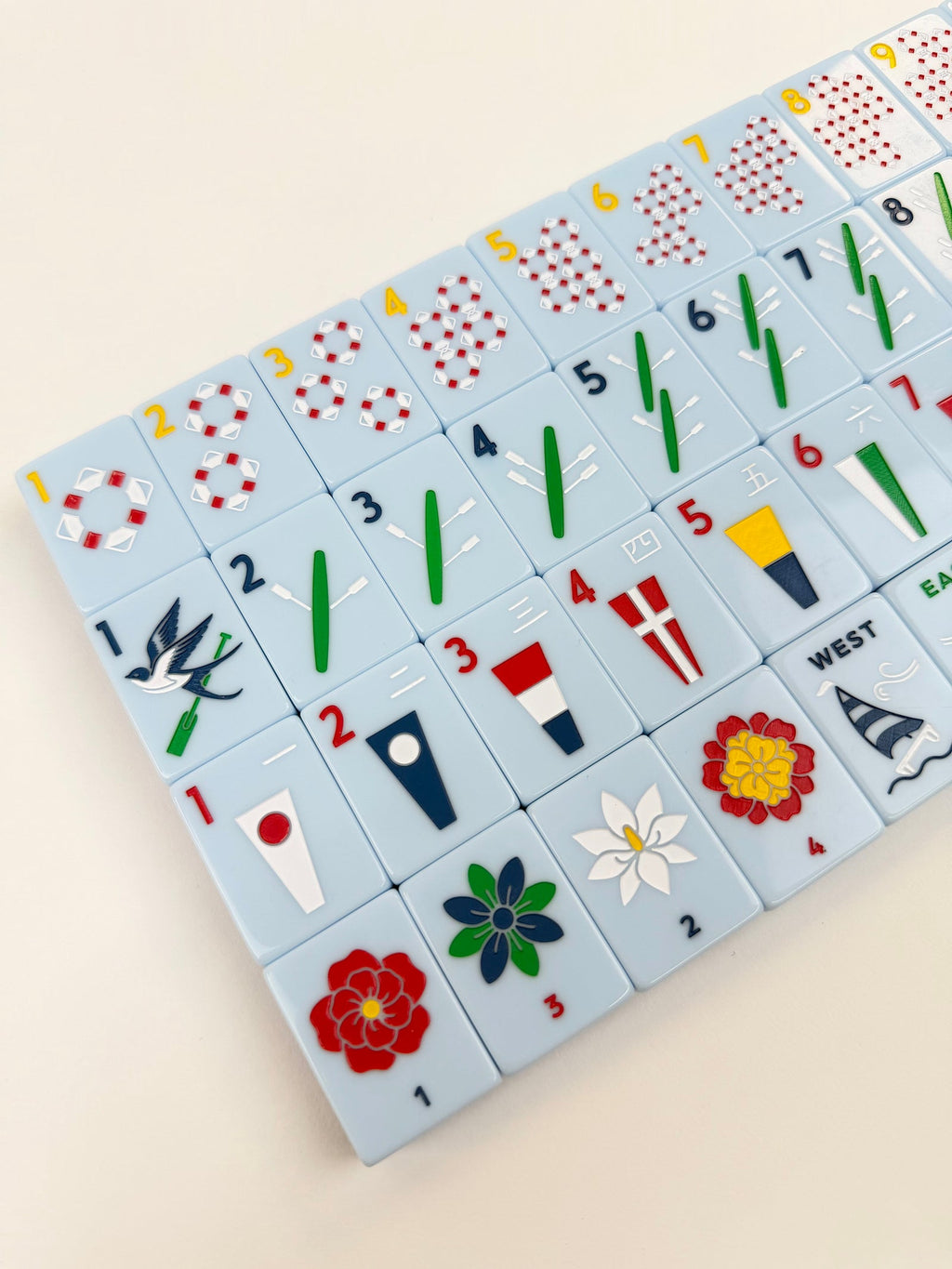 Angled close-up of Yacht Club mahjong tiles showing lifesaver dots, oar bams, signal-flag craks, and flower tiles