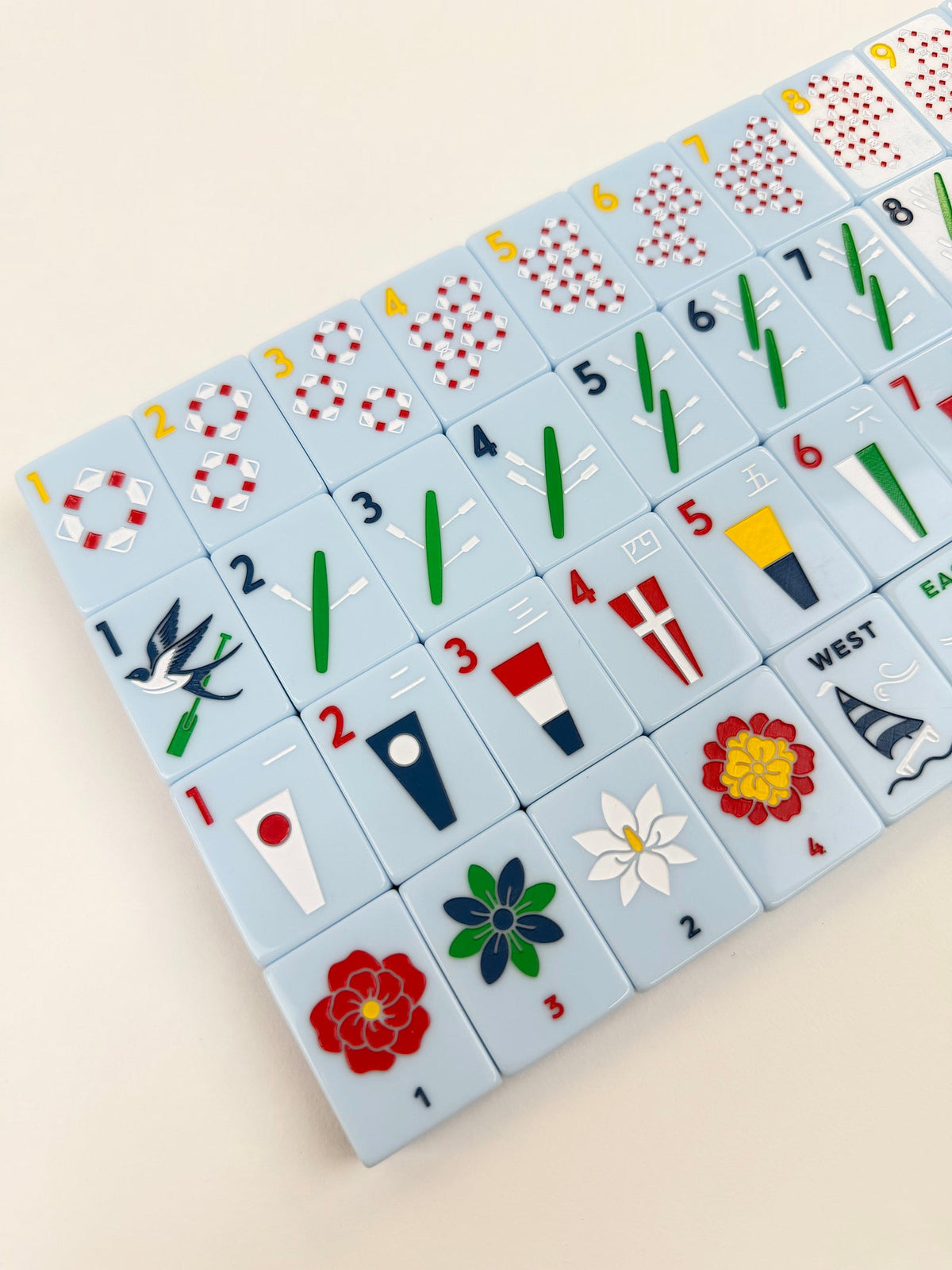 Angled close-up of Yacht Club mahjong tiles showing lifesaver dots, oar bams, signal-flag craks, and flower tiles