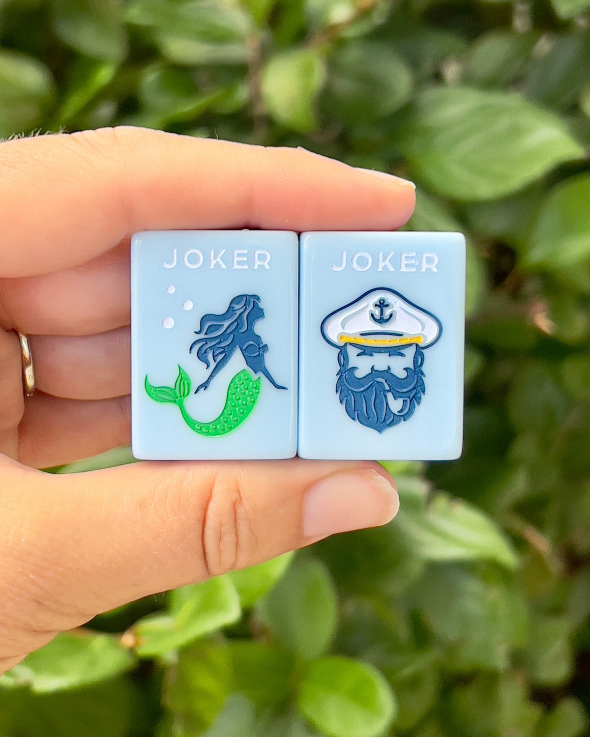 Two Yacht Club joker tiles held in hand, a green-tailed mermaid and a bearded sailor in a captain's hat
