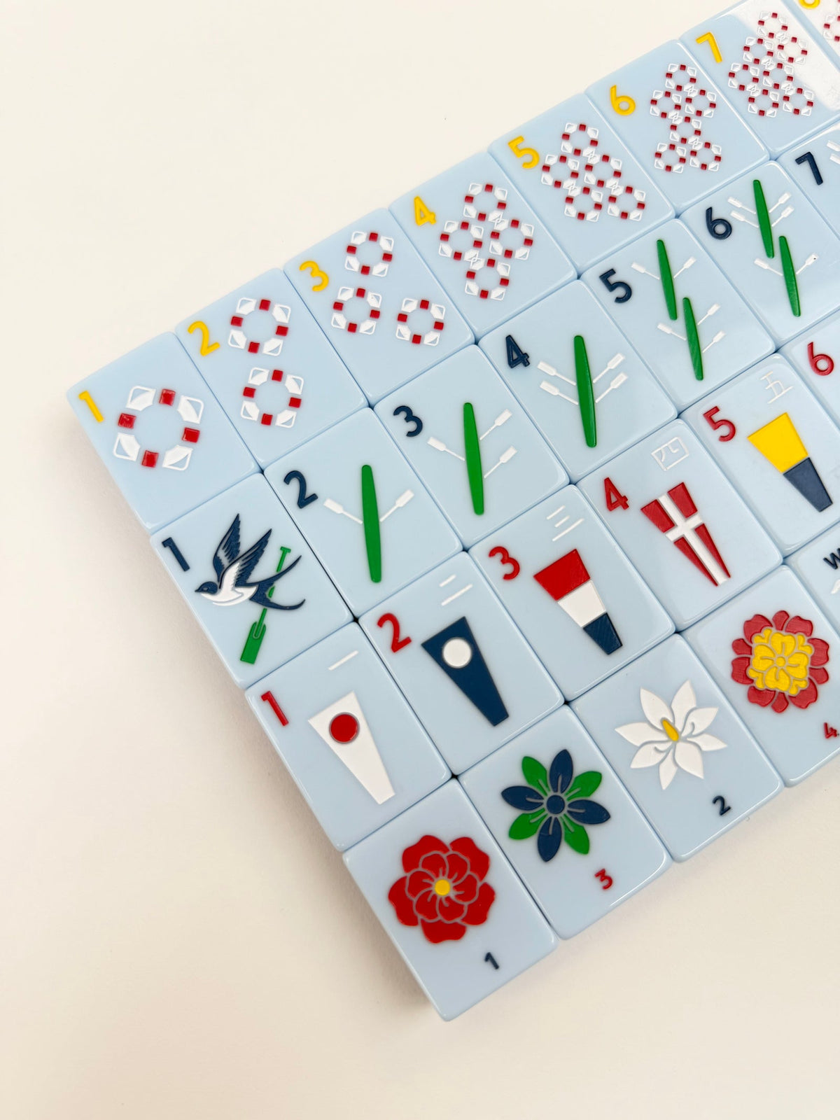 Angled view of Yacht Club mahjong tiles from the corner, showing the swallow one bam and numbered flower tiles
