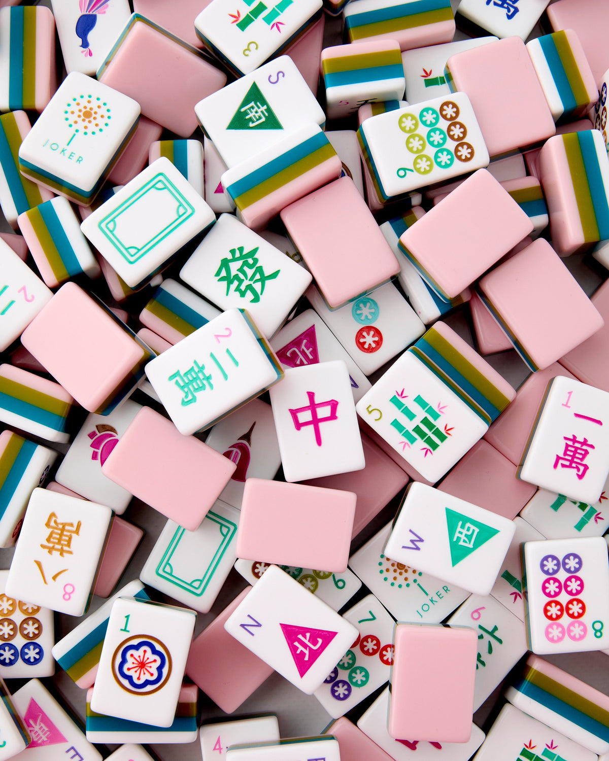 Oh My Mahjong La Fete tiles piled loosely, blush pink backs striped with olive and teal beside white tile faces