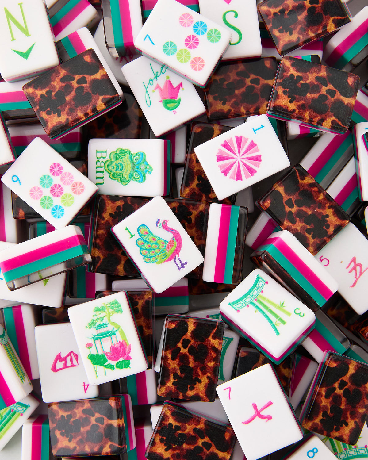 Oh My Mahjong Glow Wild tiles piled loosely, tortoiseshell backs striped with hot pink and teal beside white tile faces