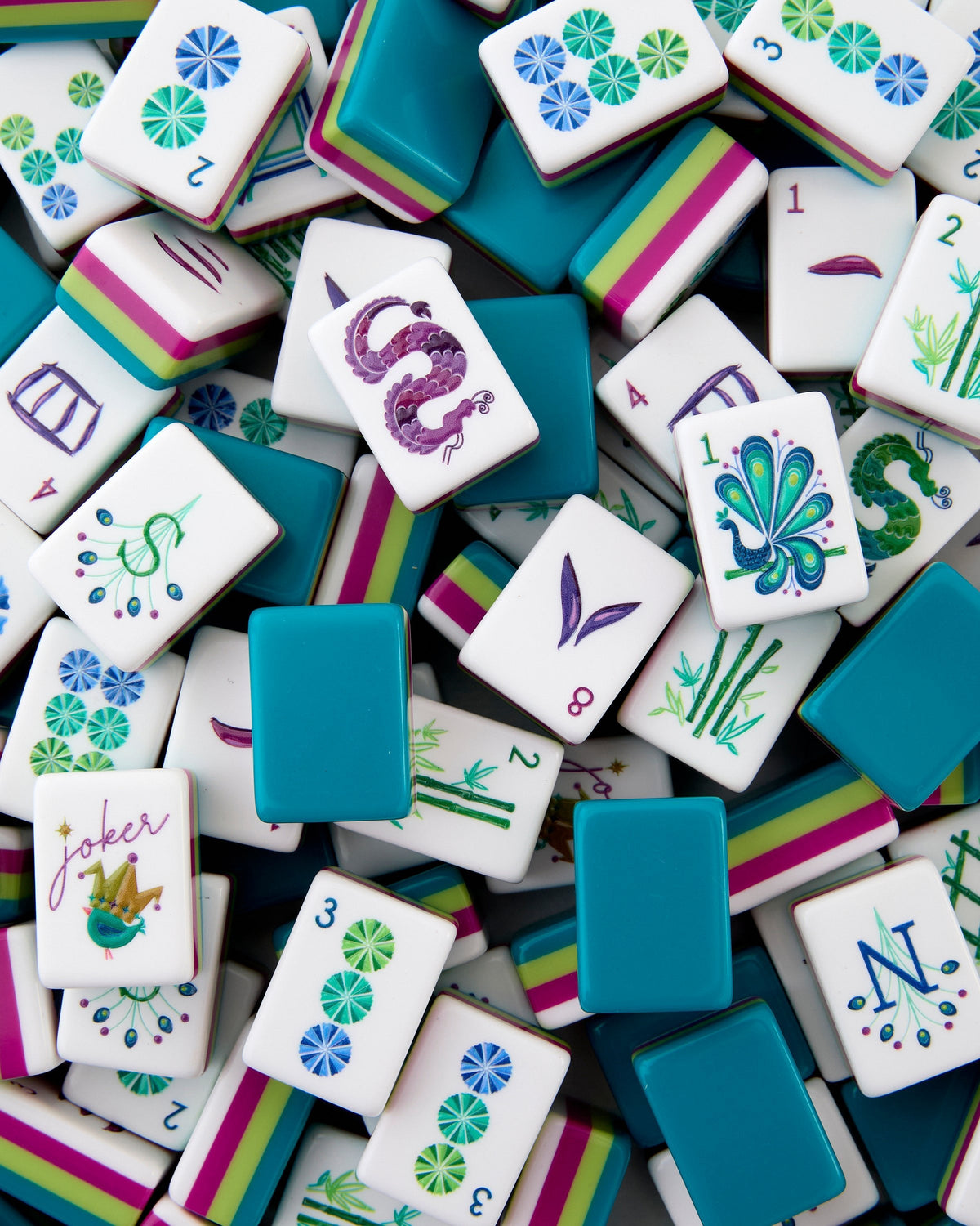 Oh My Mahjong Lagoon tiles piled loosely, teal backs striped with citron and magenta beside white tile faces