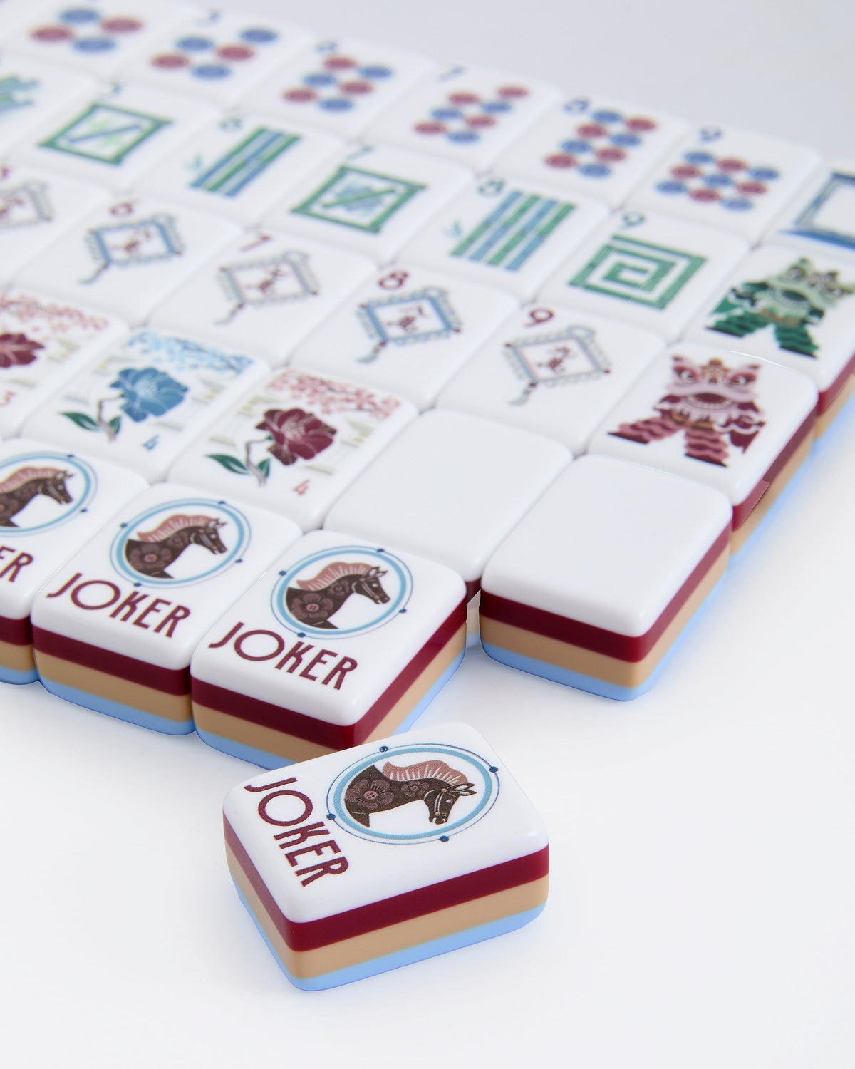 Close-up of Osler joker tiles with a horse medallion, showing the layered blue, burgundy, and tan tile edges