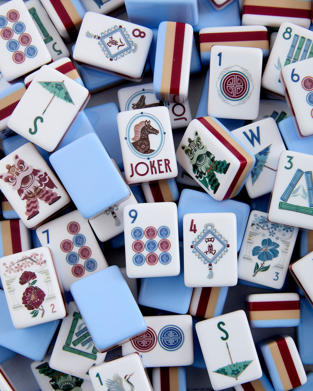 Oh My Mahjong Osler tiles piled loosely, pale blue backs striped with burgundy and tan beside white tile faces