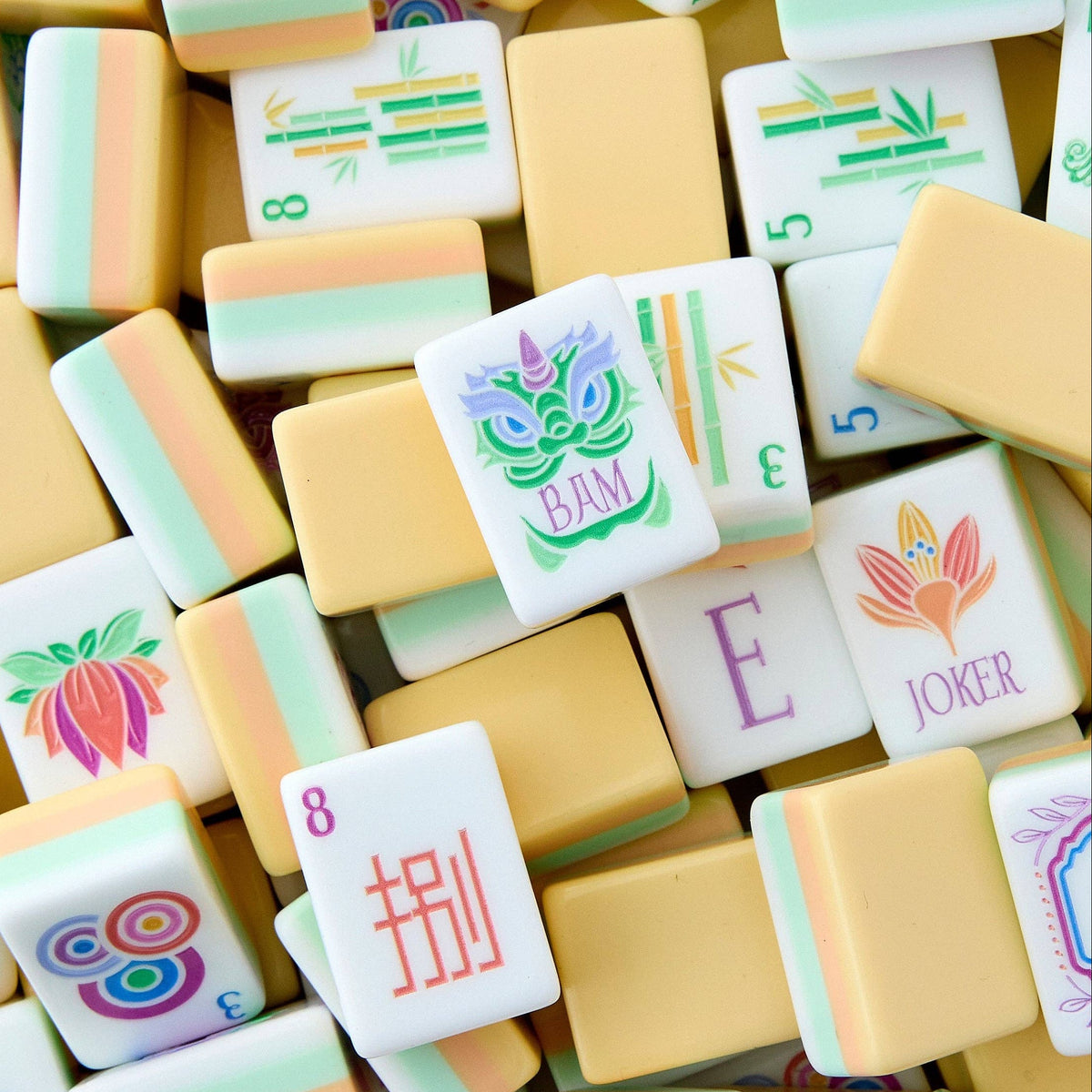 Oh My Mahjong Sorbet tiles piled loosely, butter yellow backs striped with peach and light turquoise beside white tile faces