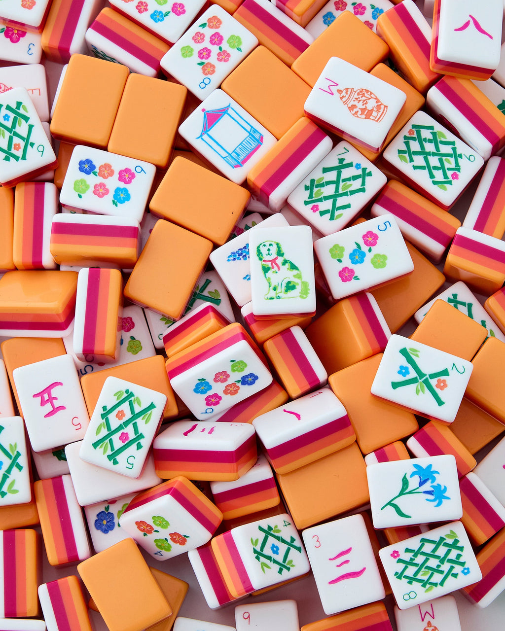 Oh My Mahjong Sunset tiles piled loosely, orange backs striped with coral and neon pink beside white tile faces