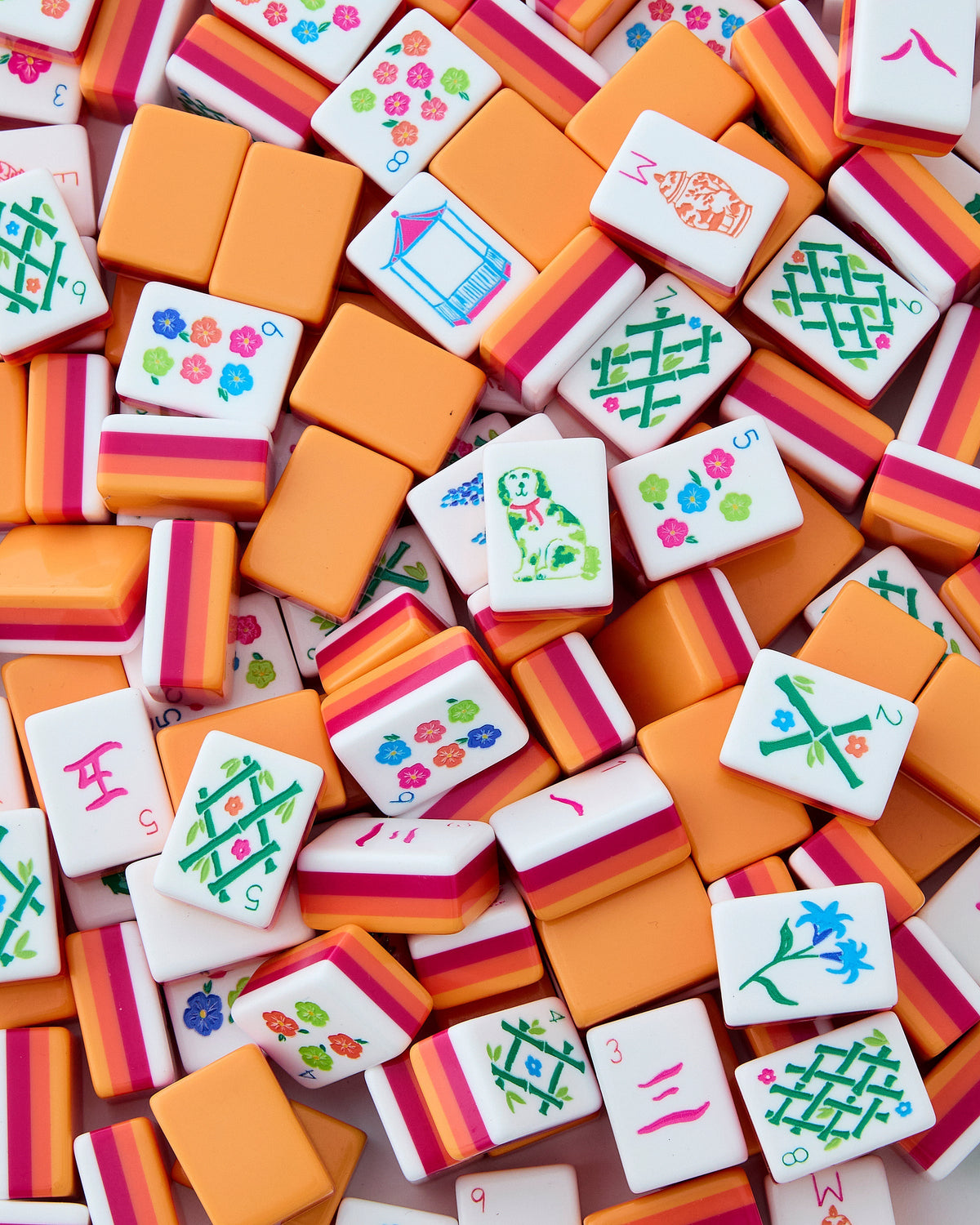 Oh My Mahjong Sunset tiles piled loosely, orange backs striped with coral and neon pink beside white tile faces
