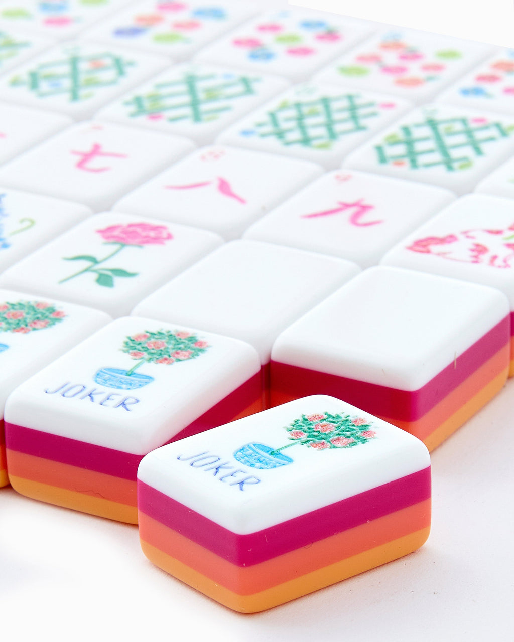 Close-up of Sunset joker tiles with a rose topiary in a blue pot, showing the layered orange, coral, and neon pink tile edges