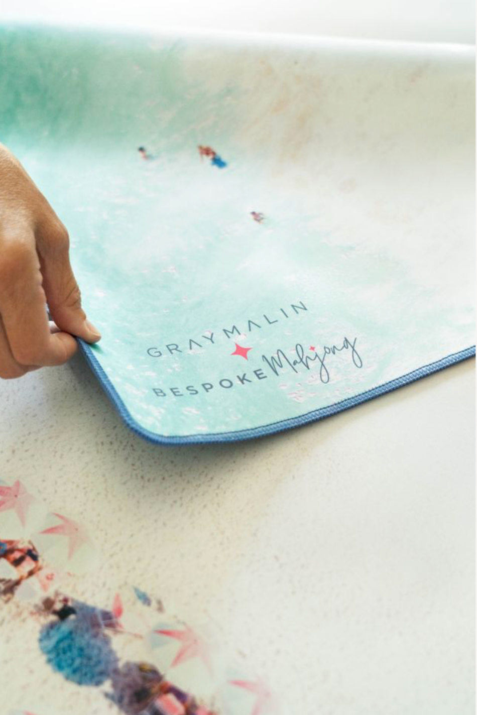Hand lifting the corner of the Gray Malin Beach Club mat to show its thickness and stitched edge